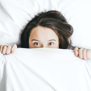 Woman pulling bed cover up to her eyes