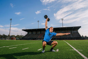Man in a squat pressing a dumbbell overhead with one hand