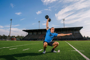 Man in a squat pressing a dumbbell overhead with one hand