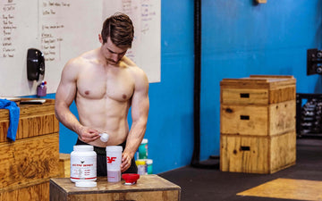 Young man pouring a scoop of Goat Whey protein powder into shaker bottle inside gym